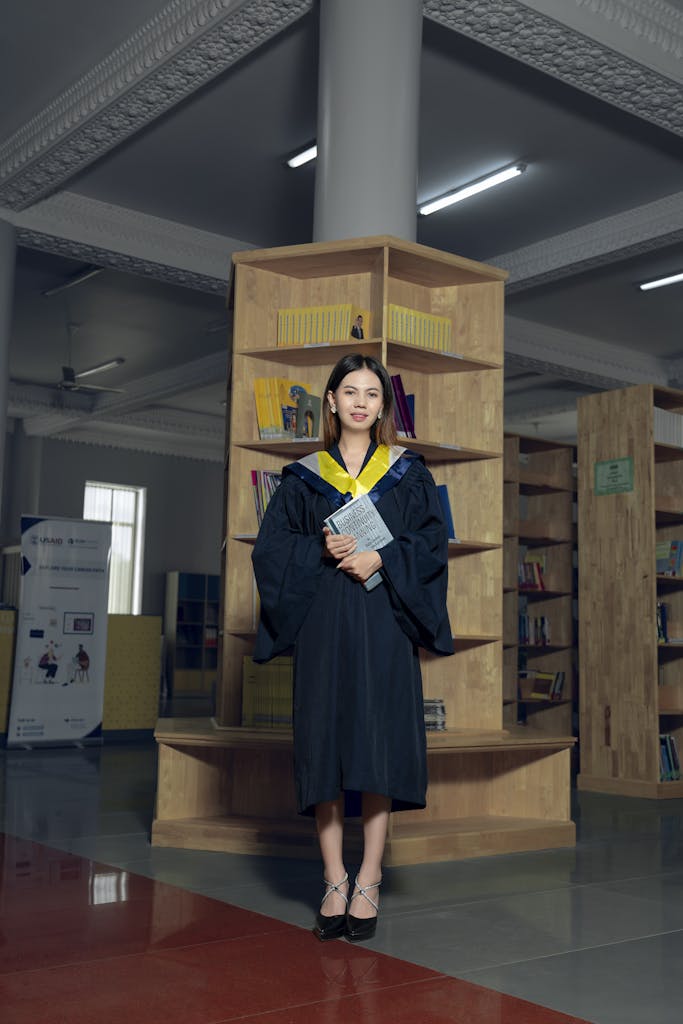 A woman in a graduation gown standing in front of a bookcase